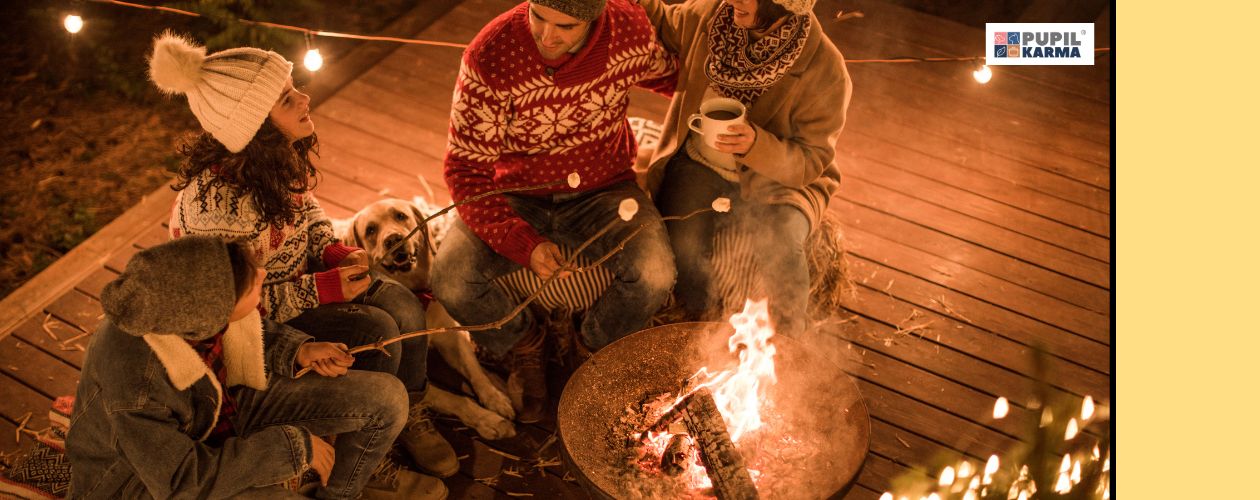 Wspólny cza. Rodzina ubrana na zimowo siedzi na tarasie. Widok z góry, światełka, ognesko i pies obok ludzi. Po prawej żółty pas i logo pupilkarma. 